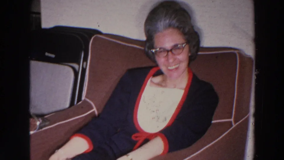 The woman smiles again from the brown upholstered seat, framed by visible 8mm borders and interior furnishings in the 1966 clip.