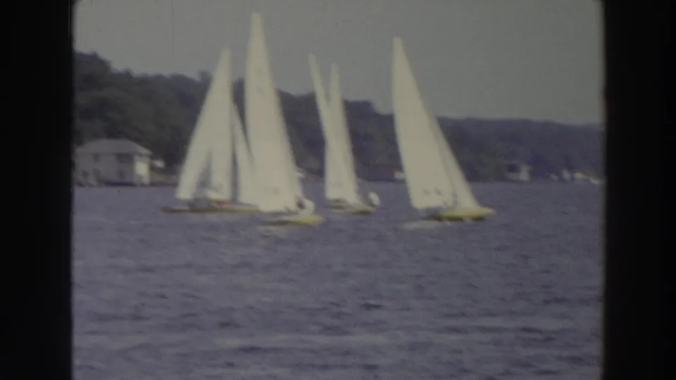 1966 Madison, Wisconsin 8mm frame showing a cluster of small sailboats on a lake with a wooded shoreline behind them.