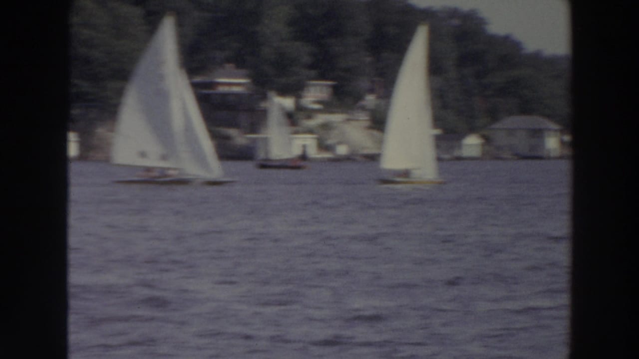 1966 Madison, Wisconsin lake scene with white-sailed dinghies, rippled water, wooded shore, and distant lakeside structures.
