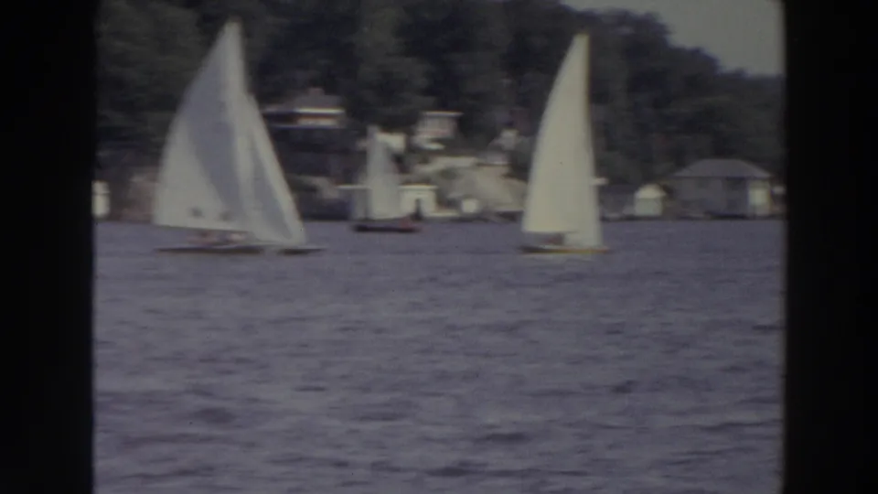 1966 Madison, Wisconsin lake scene with white-sailed dinghies, rippled water, wooded shore, and distant lakeside structures.