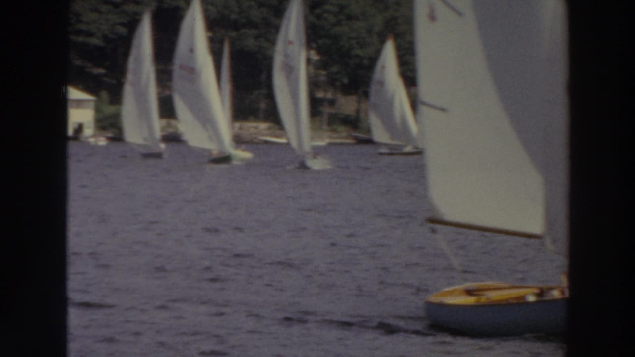 1966 Madison, Wisconsin 8mm frame showing several white sailboats on a lake with trees and shoreline buildings in the distance.