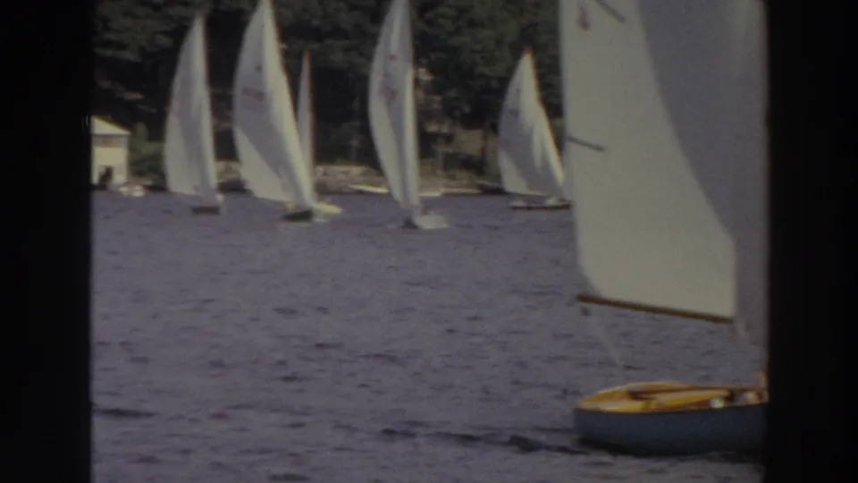 1966 Madison, Wisconsin 8mm frame showing several white sailboats on a lake with trees and shoreline buildings in the distance.