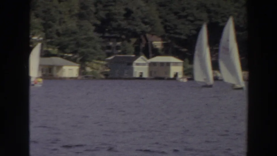 1966 Madison, Wisconsin frame with a sailboat close to camera and additional white sails near tree-lined lakeside homes.