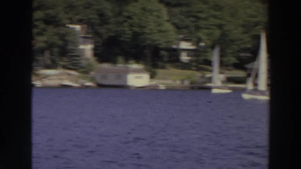 1966 Madison, Wisconsin frame with sailboats at right and lakeside homes, docks, and trees across the water.