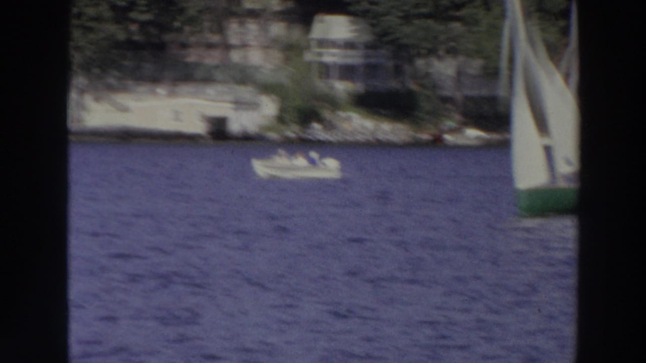 Lake view with shoreline homes, a small motorboat, and part of a sailboat at right.
