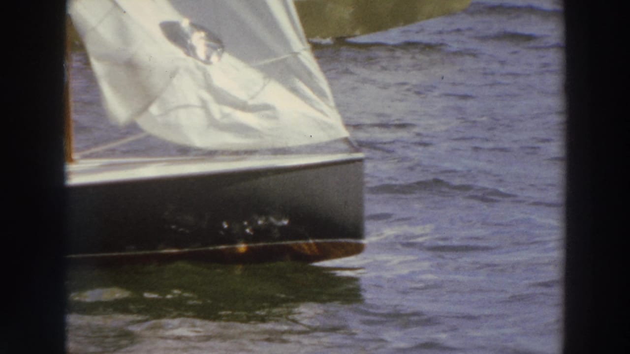 Close view of a small sailboat with a white sail moving across choppy lake water.
