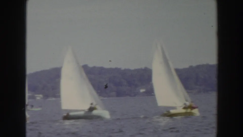 1966 Madison, Wisconsin 8mm frame showing two small sailboats heeling on choppy water during a windy lake outing.