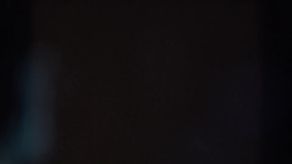 Very dark 8mm frame showing faint blue flare at lower left and subtle brown-black exposure variation.