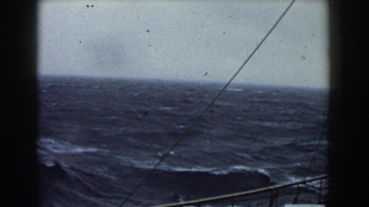 Large dark wave and white spray beyond ship railings under a gray sky.