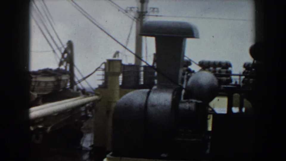 Deck-level 8mm frame with rigging, railings, a lifeboat, and dark ship machinery silhouetted against the sea.