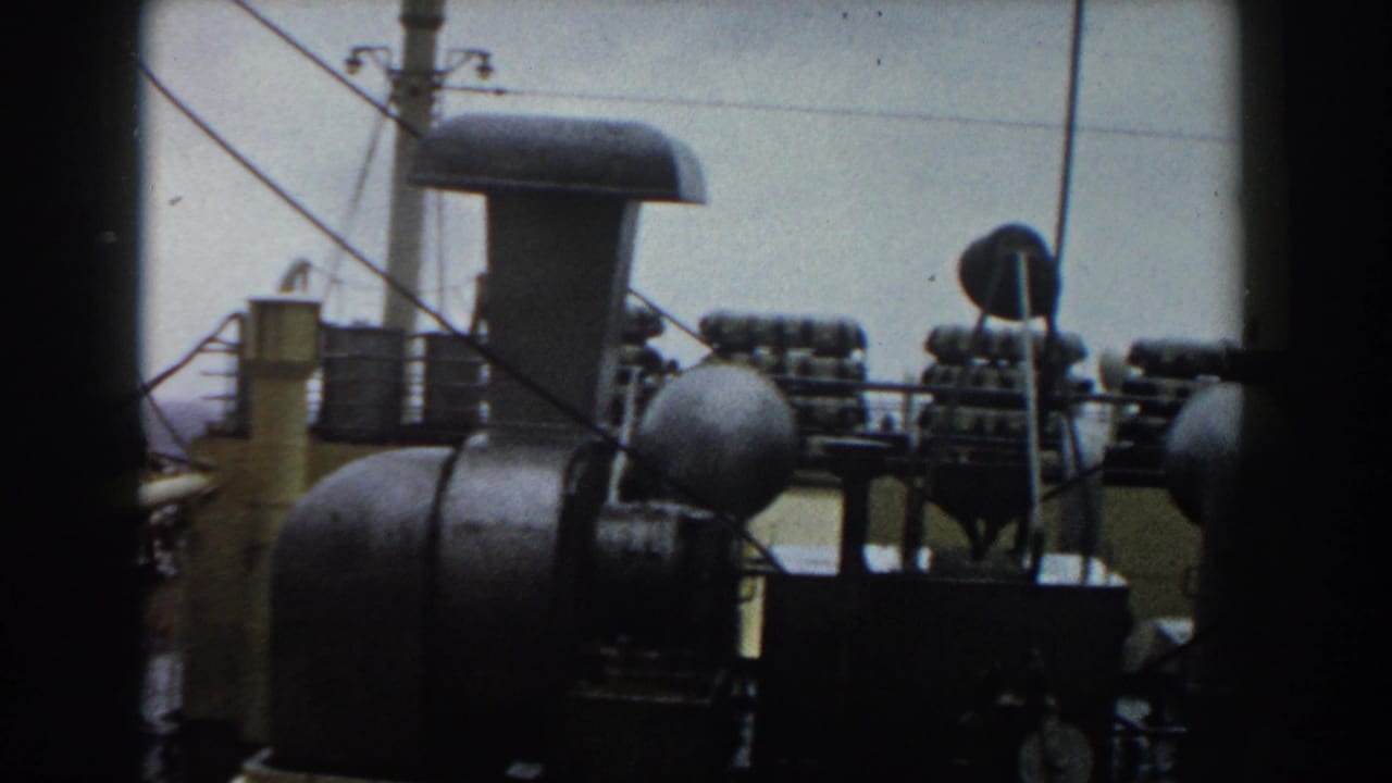 1959 8mm frame showing ship deck equipment, cables, vents, and ocean horizon from a traveler’s viewpoint.