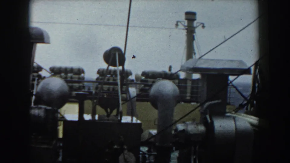 A shipboard view with railings, cables, rounded deck fittings, and the sea visible beyond the vessel.