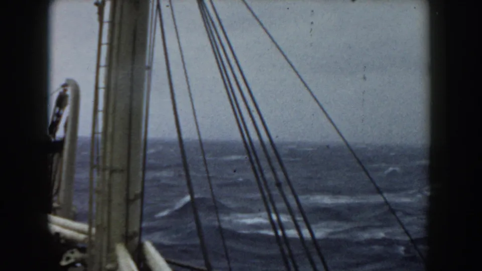 A closer aboard-vessel view shows mast rigging and the deck edge with rough open ocean and scattered whitecaps beyond.