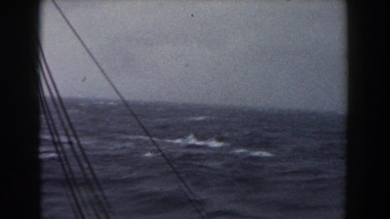 1959 8mm frame of stormy Atlantic water viewed from a ship window, with rigging lines crossing the left side.