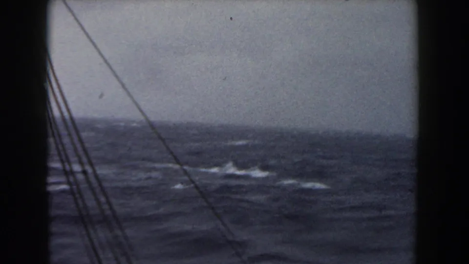 1959 8mm frame of stormy Atlantic water viewed from a ship window, with rigging lines crossing the left side.