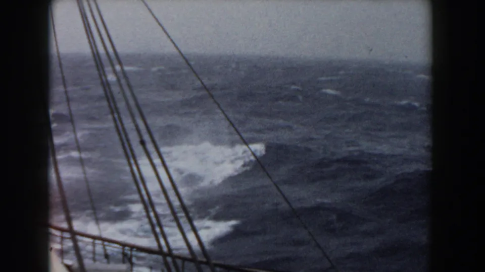 Rough open water with whitecaps appears beyond mast rigging from an 8mm home-movie view aboard a sailing vessel.
