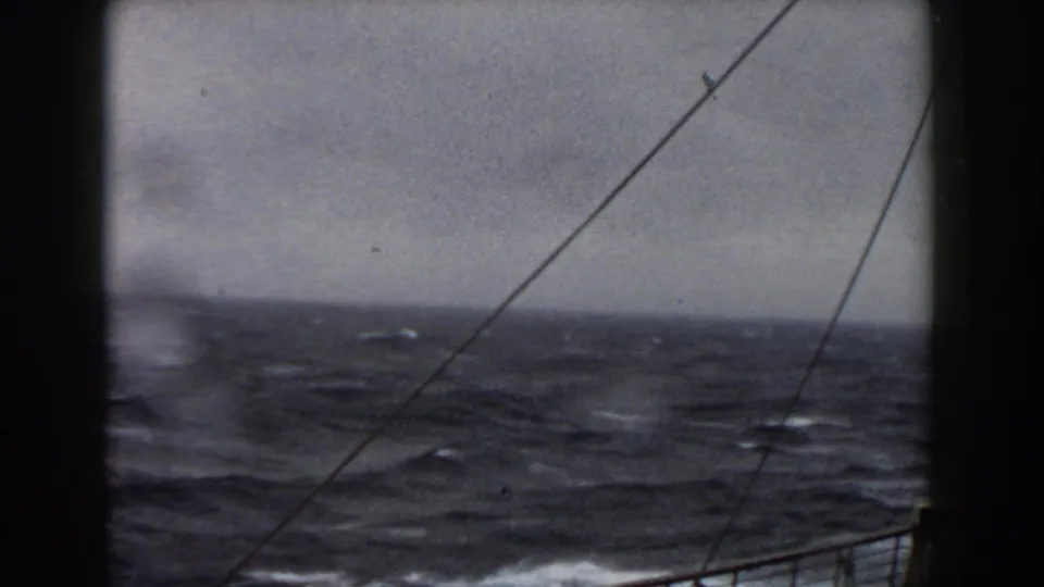 Shipboard 8mm frame showing rough Atlantic seas, a low horizon, rigging lines, and part of the vessel structure at right.