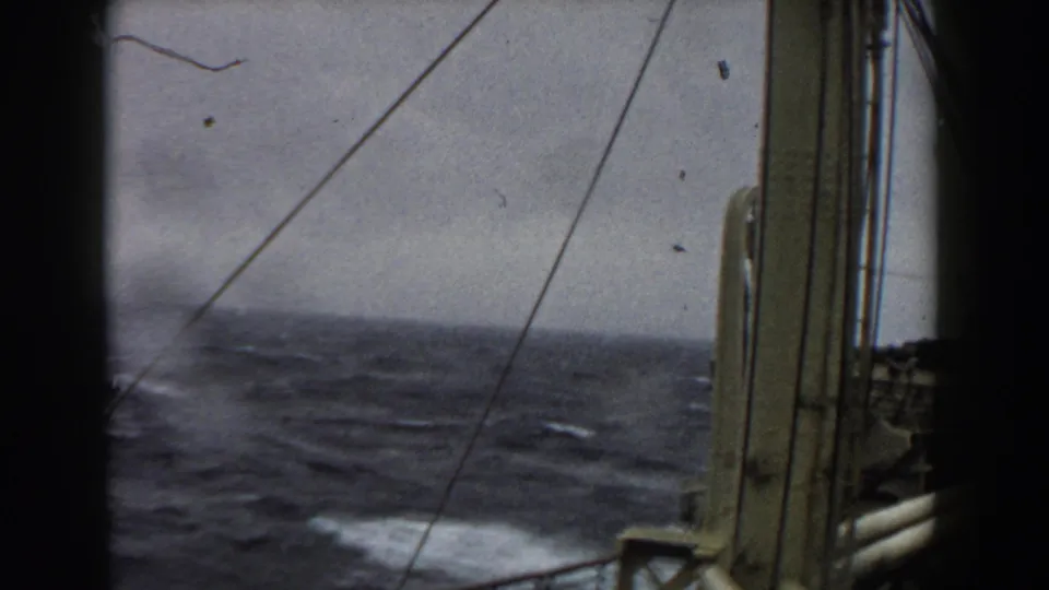 Final shipboard frame shows dark rough seas, a patch of white spray, rigging, railing, and vessel structure at the right edge.