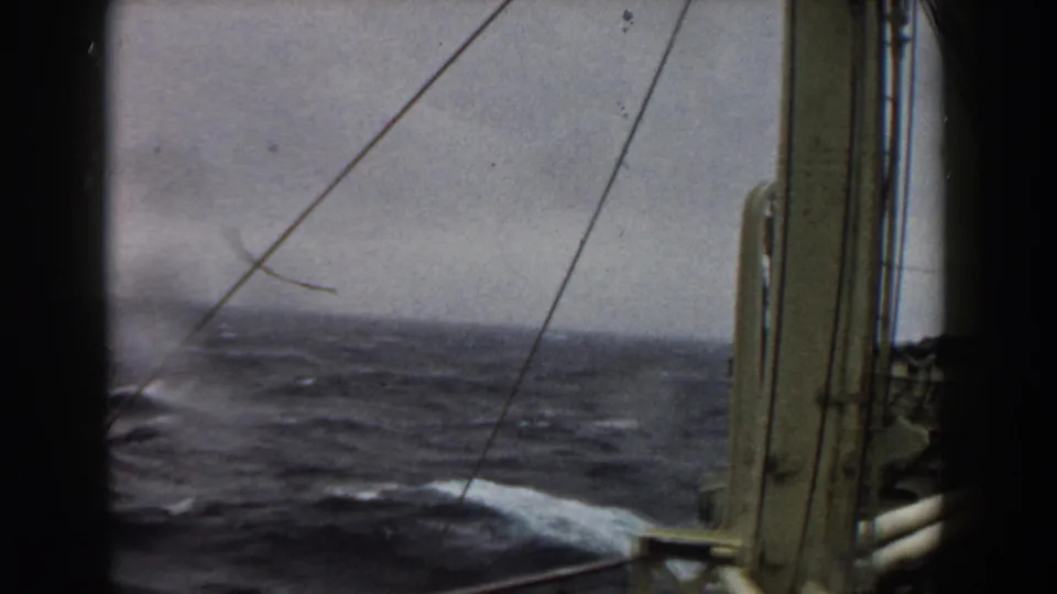 Rough ocean waves and whitecaps seen from a ship through rigging lines and vertical deck structure in archival 8mm footage from 1959.