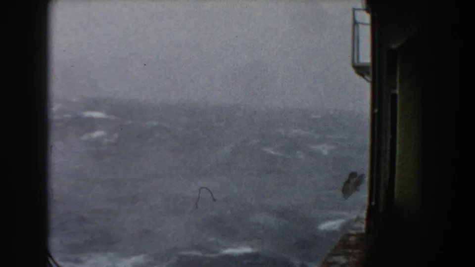 A softer, more blurred 8mm frame shows rough open water and white streaks of wave foam beside the dark edge of shipboard structure.