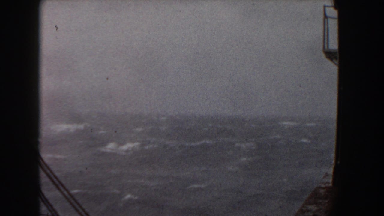 Rough ocean waves seen from a ship with dark rigging at the edge of the frame.