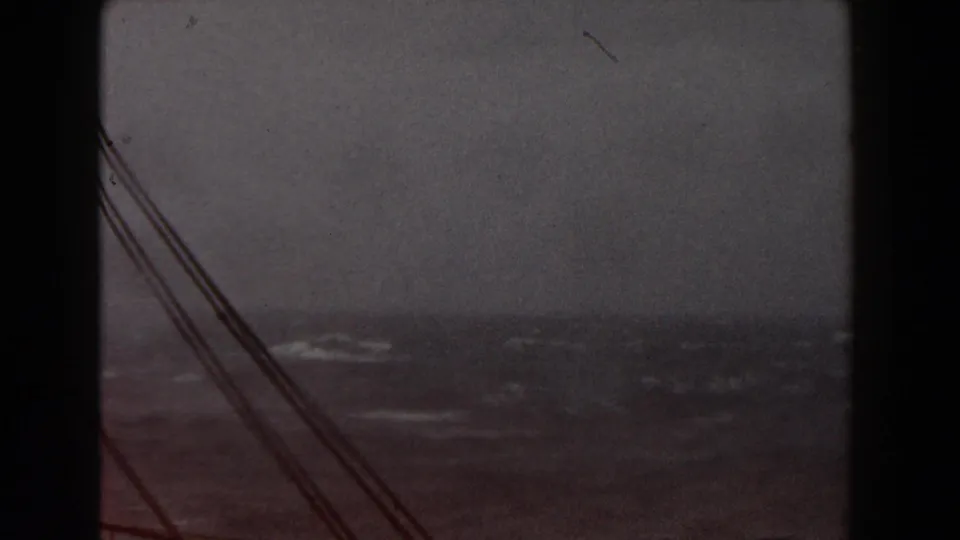 Shipboard 8mm view of choppy Atlantic water, with a dark vertical structure and rigging lines cutting across the cloudy horizon.