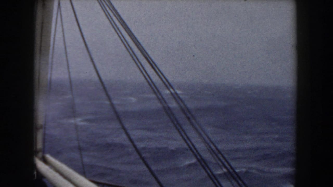 Dark rigging lines and a rail cross a gray-blue ocean with whitecaps in the distance.