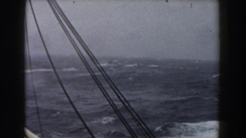 Handheld 8mm view of diagonal rigging above choppy sea, with white foam and a hazy horizon visible.