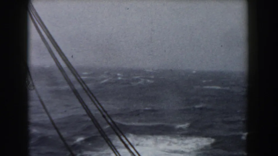 Darker 8mm frame from a sailing vessel, showing rigging over turbulent ocean water under a muted sky.
