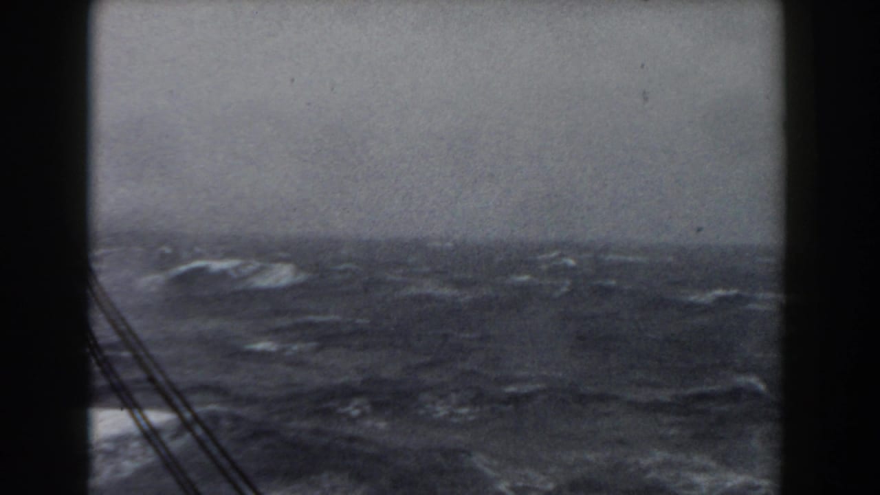 Choppy sea and gray horizon framed by dark vertical ship structure and rigging.
