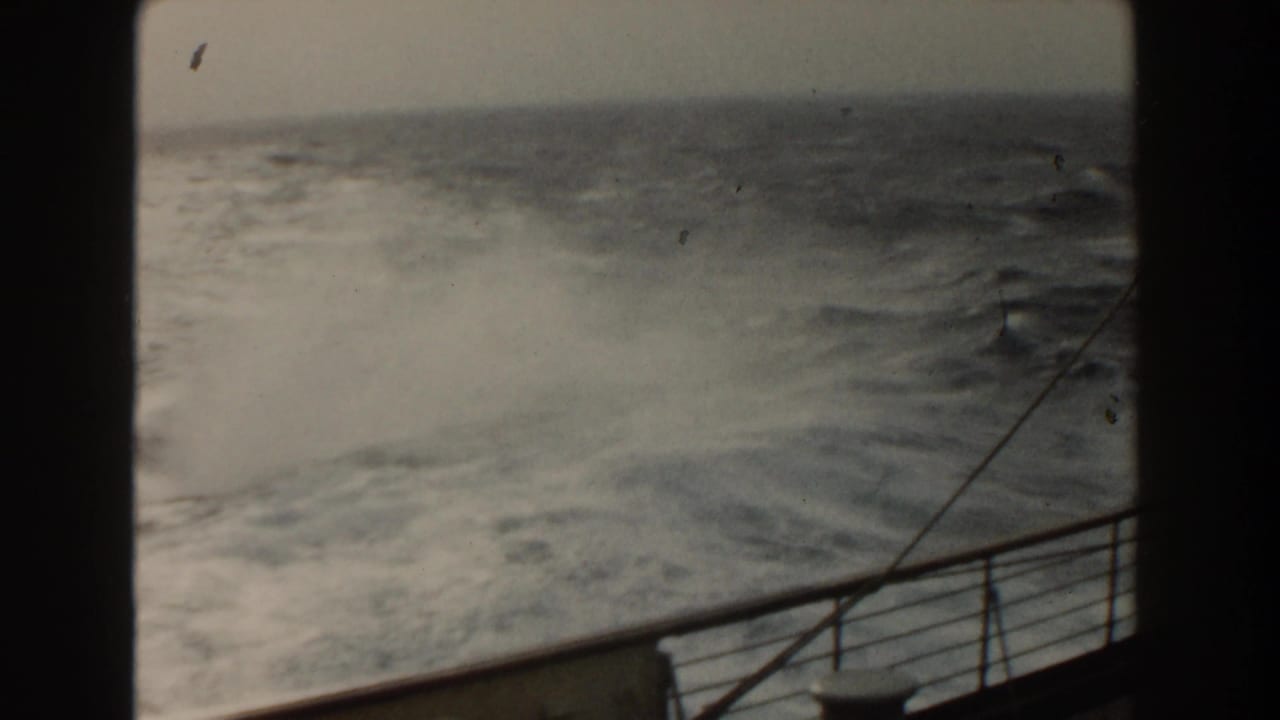 1959 8mm view from a ship deck toward rough Atlantic water, with railing, spray, and a dark film border visible.