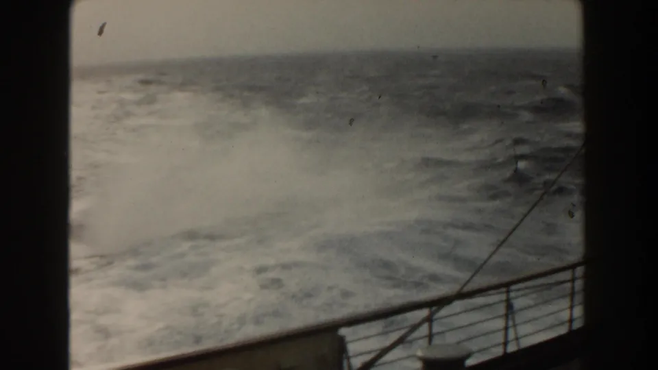 1959 8mm view from a ship deck toward rough Atlantic water, with railing, spray, and a dark film border visible.