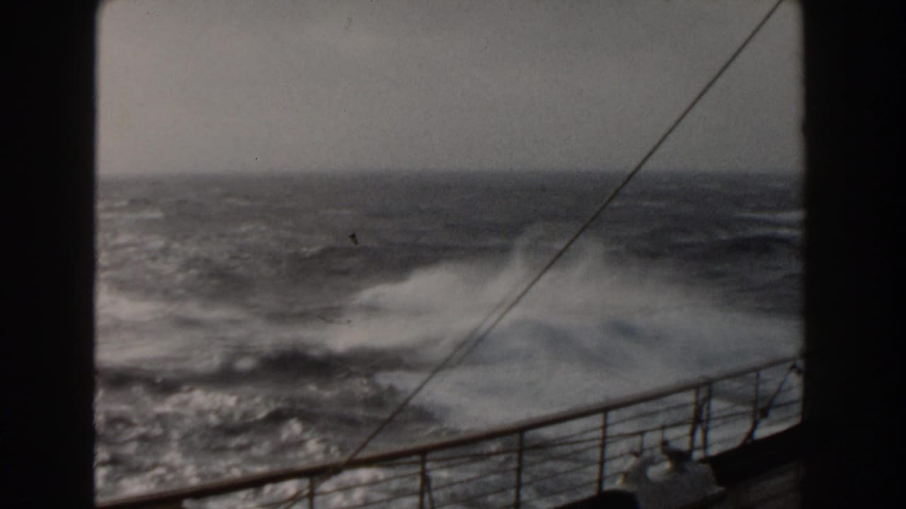 Rough ocean waves seen past ship railing and diagonal rigging lines.