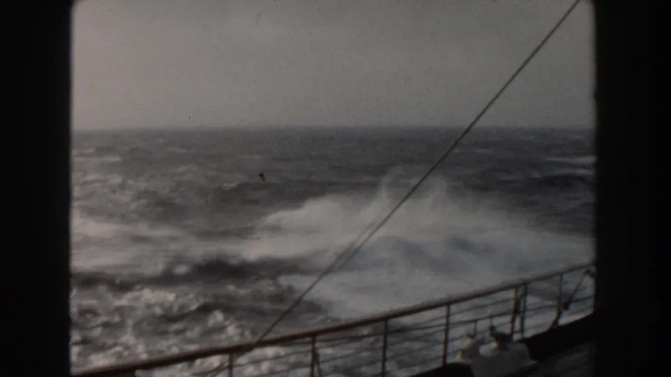 1959 8mm shipboard view of dark Atlantic waves and spray beyond deck railing under a gray horizon.