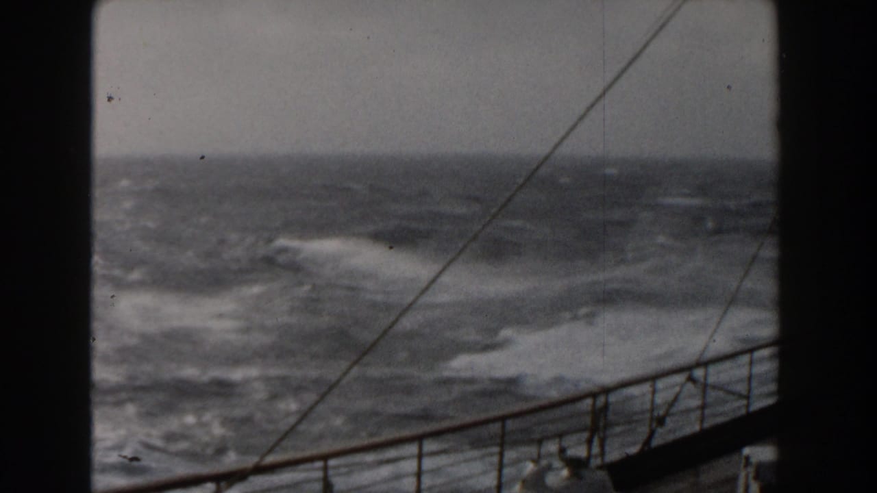 Choppy sea and foam beyond a ship railing under a gray sky.