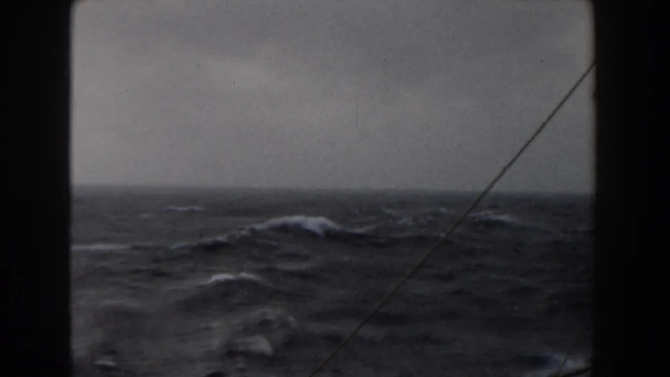 Muted 8mm view of dark open-ocean swells and whitecaps, likely filmed from a ship during rough weather.