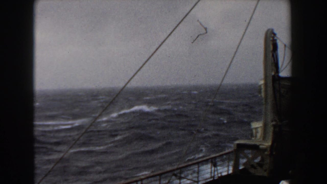 Rough ocean water seen past ship rigging and deck railings under a gray sky.