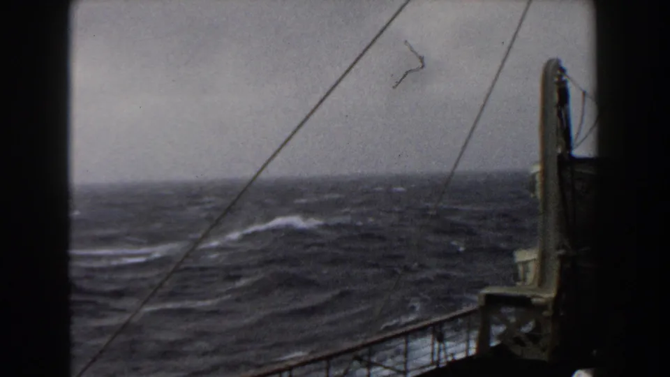 1959 8mm home-movie frame looking from a ship deck toward dark Atlantic waves, whitecaps, rigging lines, and railings.
