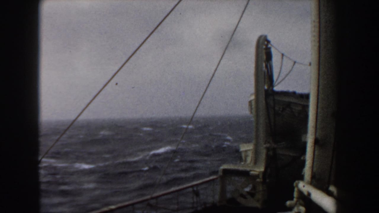 Open sea with whitecaps framed by a ship deck, railing, and vertical rigging.
