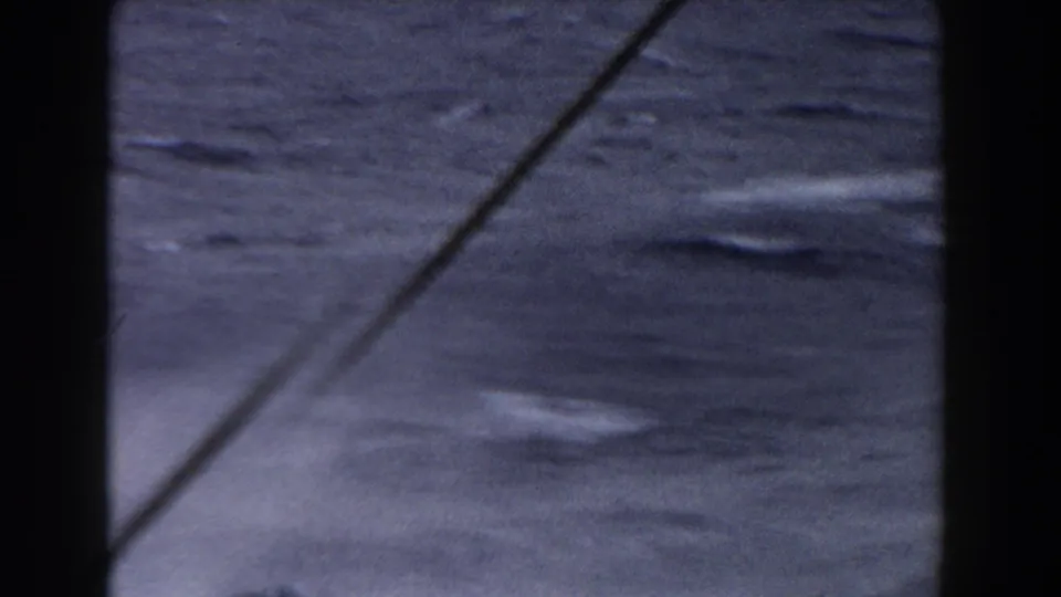 Close 8mm view of rough Atlantic water with white foam streaks and a diagonal rigging line crossing the shot.