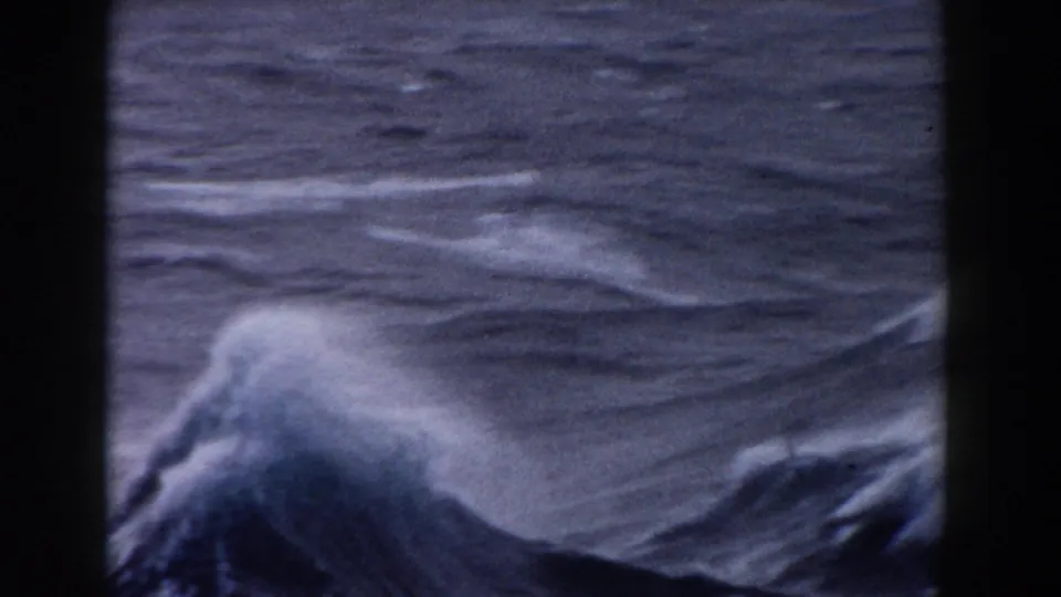 A 1959 8mm boatboard view appears to show rough Atlantic waves and white spray framed by dark vertical vessel structure.
