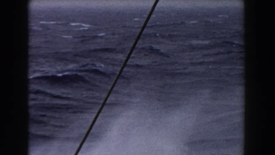 A choppy ocean surface fills the frame, with a diagonal pole or cable and dark boat structure visible in the foreground.