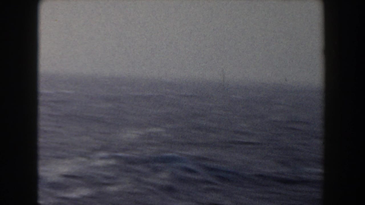 Dark ocean waves seen through a ship window or frame with a hazy horizon.