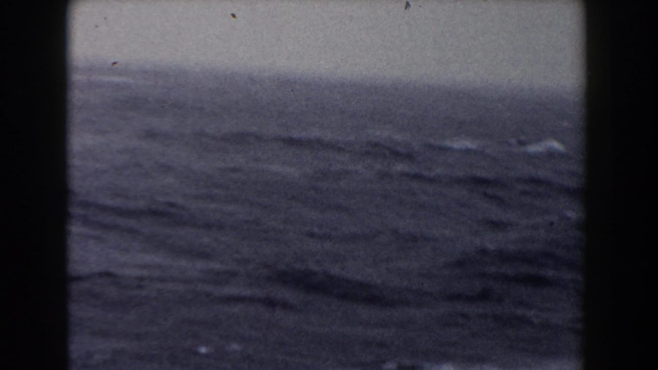 Open sea with rolling dark waves framed by black vertical film or ship edges.