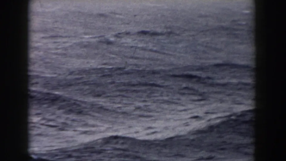 1959 8mm frame showing rippled Atlantic Ocean water and rolling swells viewed through dark boat or window edges.