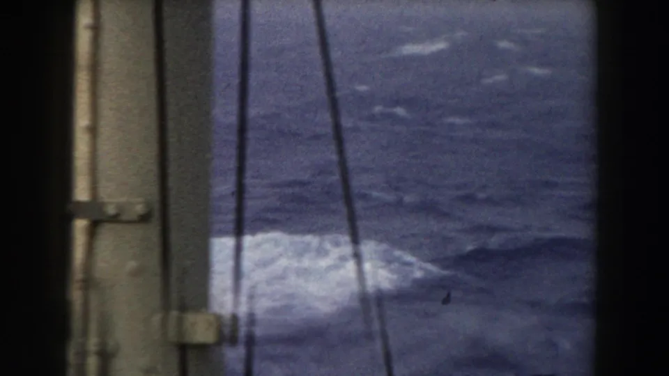 A vertical boat structure and thin lines partially obscure a view of rough blue Atlantic water with white foam below.