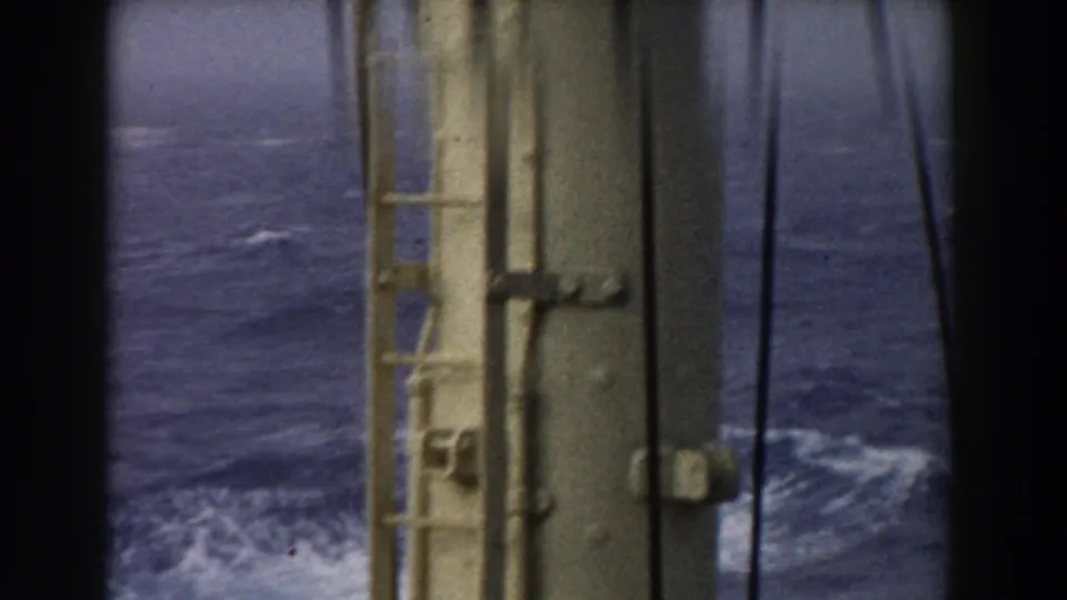 1959 8mm home-movie frame looking over choppy Atlantic water through shipboard metal framework and dark vertical framing.