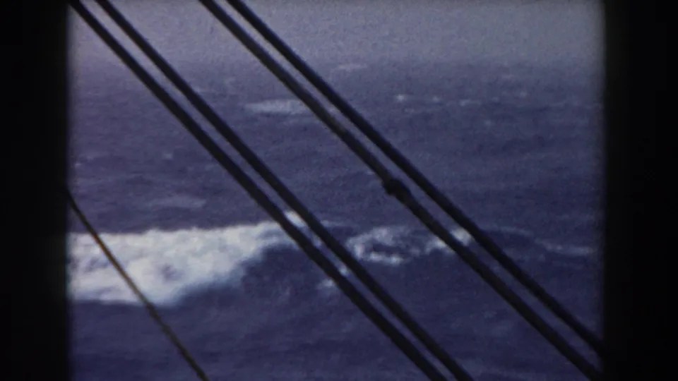 Foam and rough sea pass below diagonal ship rigging, with soft focus and faded color from the 8mm scan.