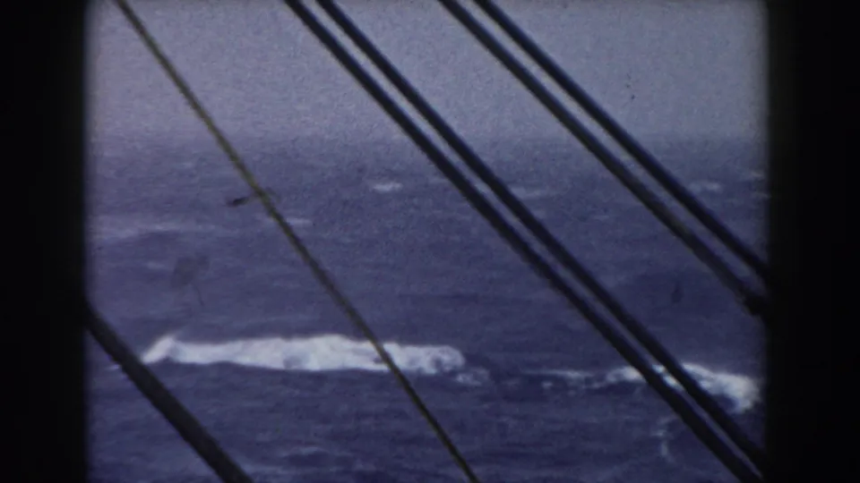 Dark Atlantic water and white foam patches are seen beneath diagonal ship rigging in a handheld 1959 8mm travel frame.