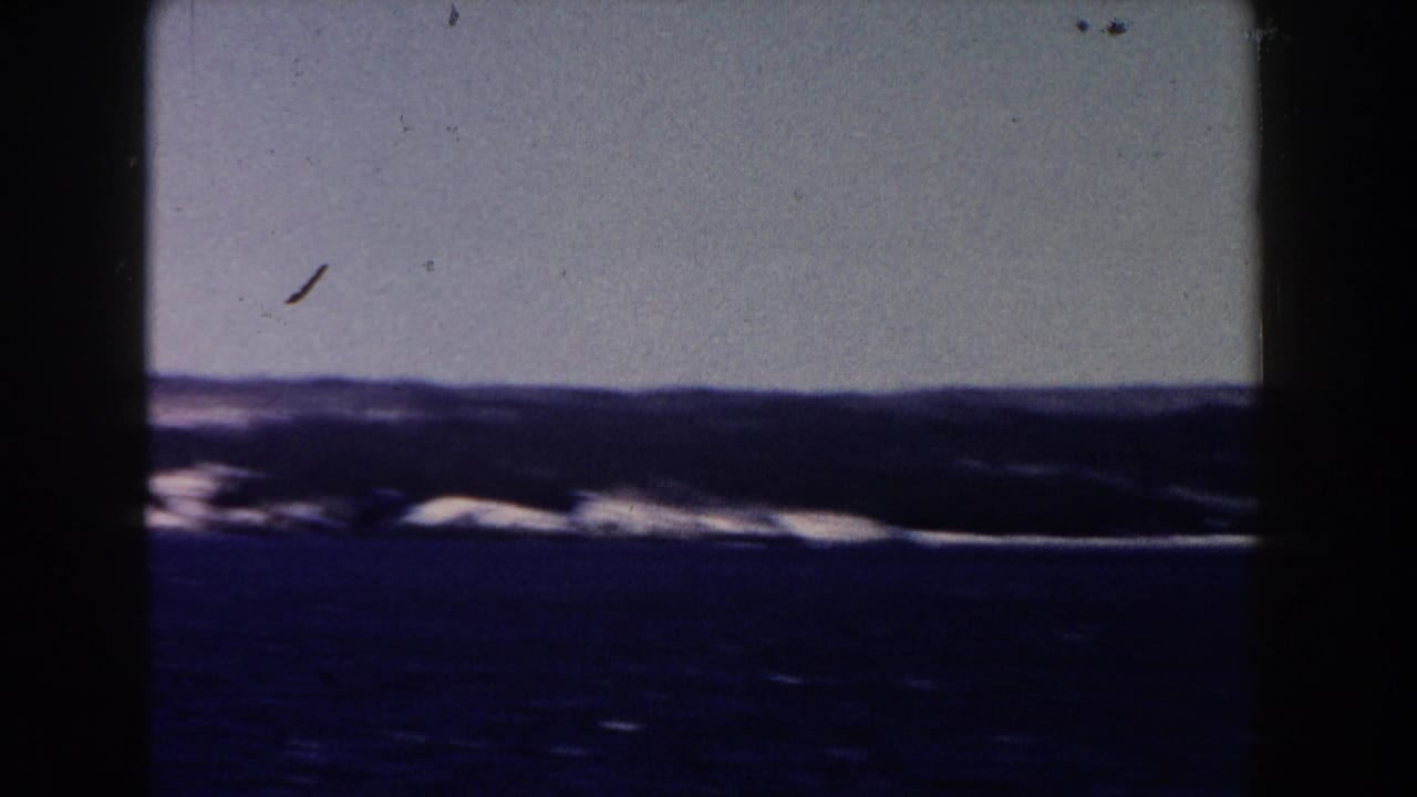 Dark water with white surf under a pale sky, framed by black film edges.